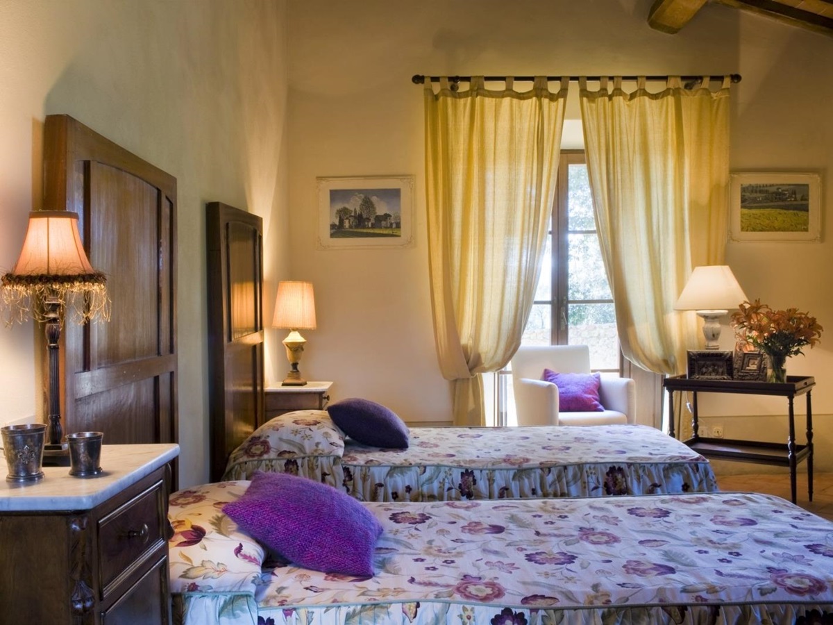 Twin room with twin beds, bedside tables, lamps, flowers and armchair at La Gavelli in Tuscany, Italy
