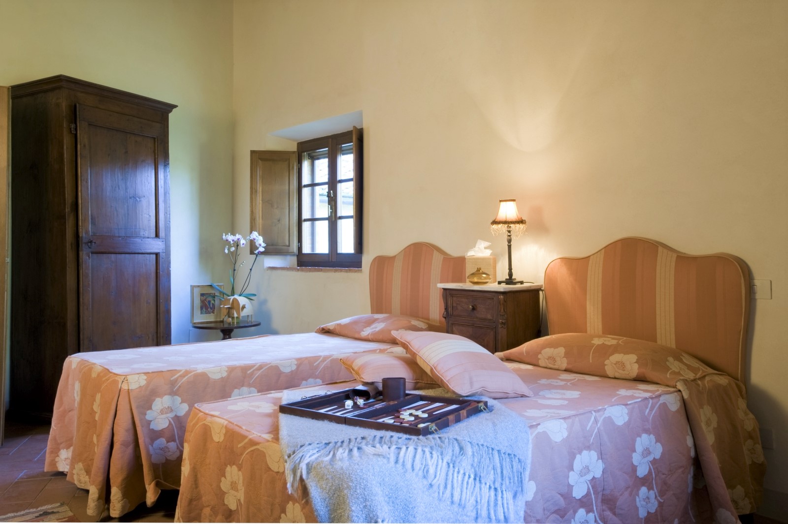 Twin room with twin beds, bedside table, lamp, flowers, wardrobe and game at La Gavelli in Tuscany, Italy