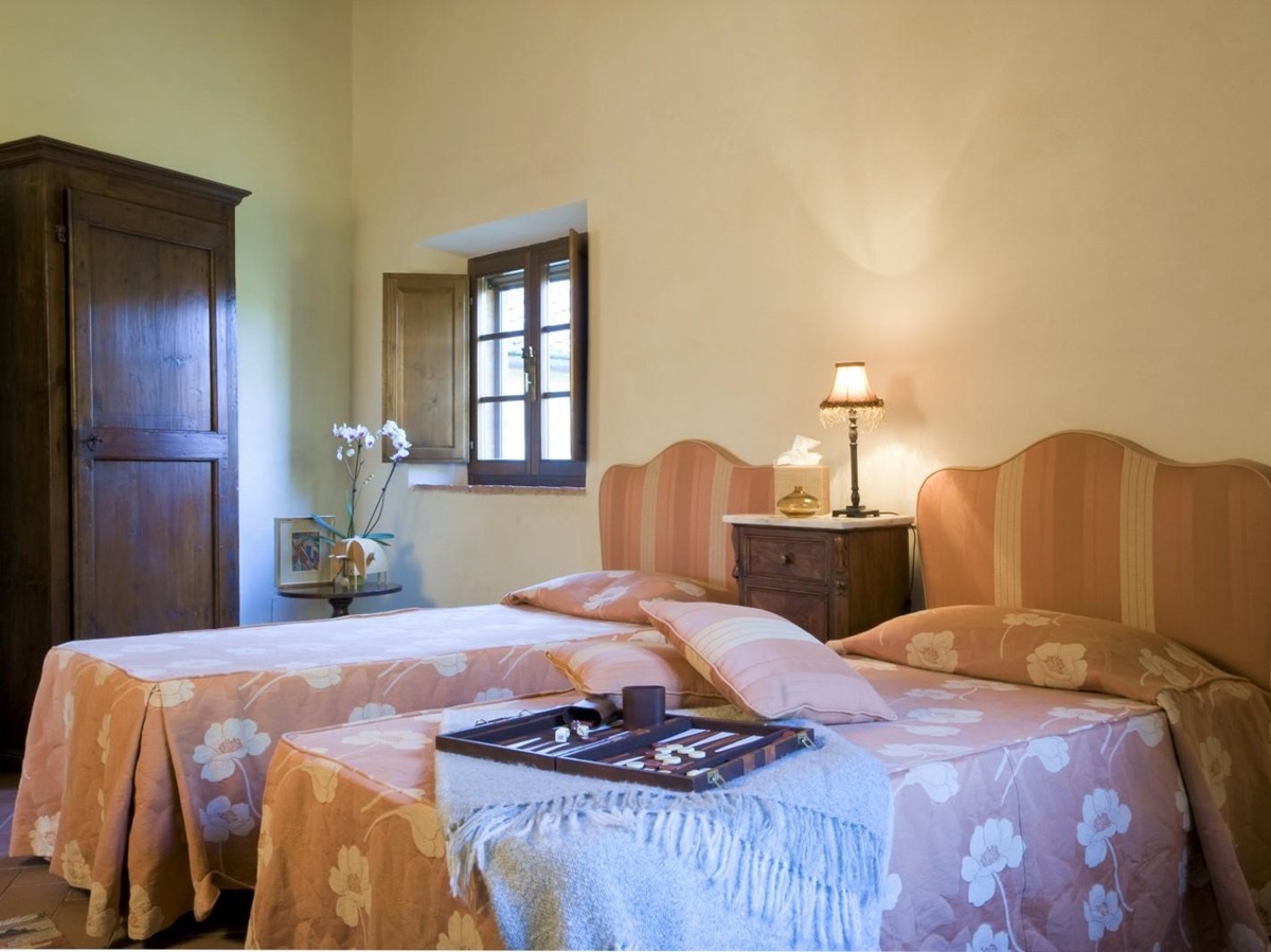 Twin room with twin beds, bedside table, lamp, flowers, wardrobe and game at La Gavelli in Tuscany, Italy