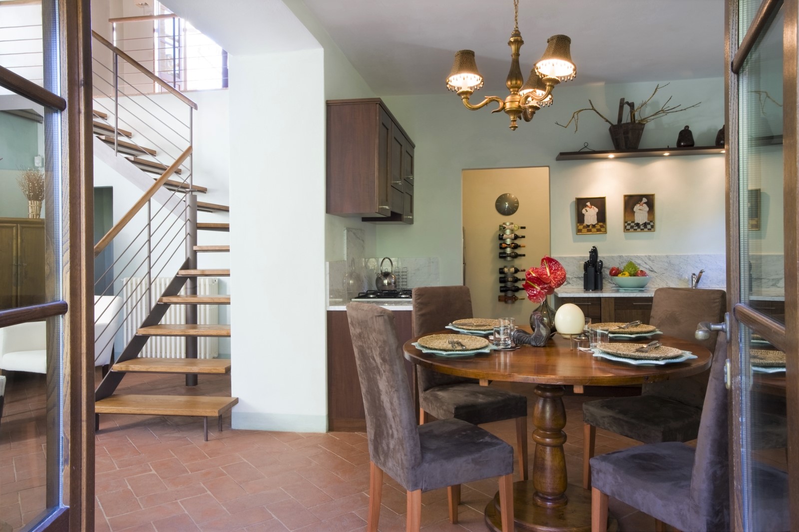 Open plan kitchen and dining area with table, chairs, hanging light and wine store at La Gavelli in Tuscany, Italy