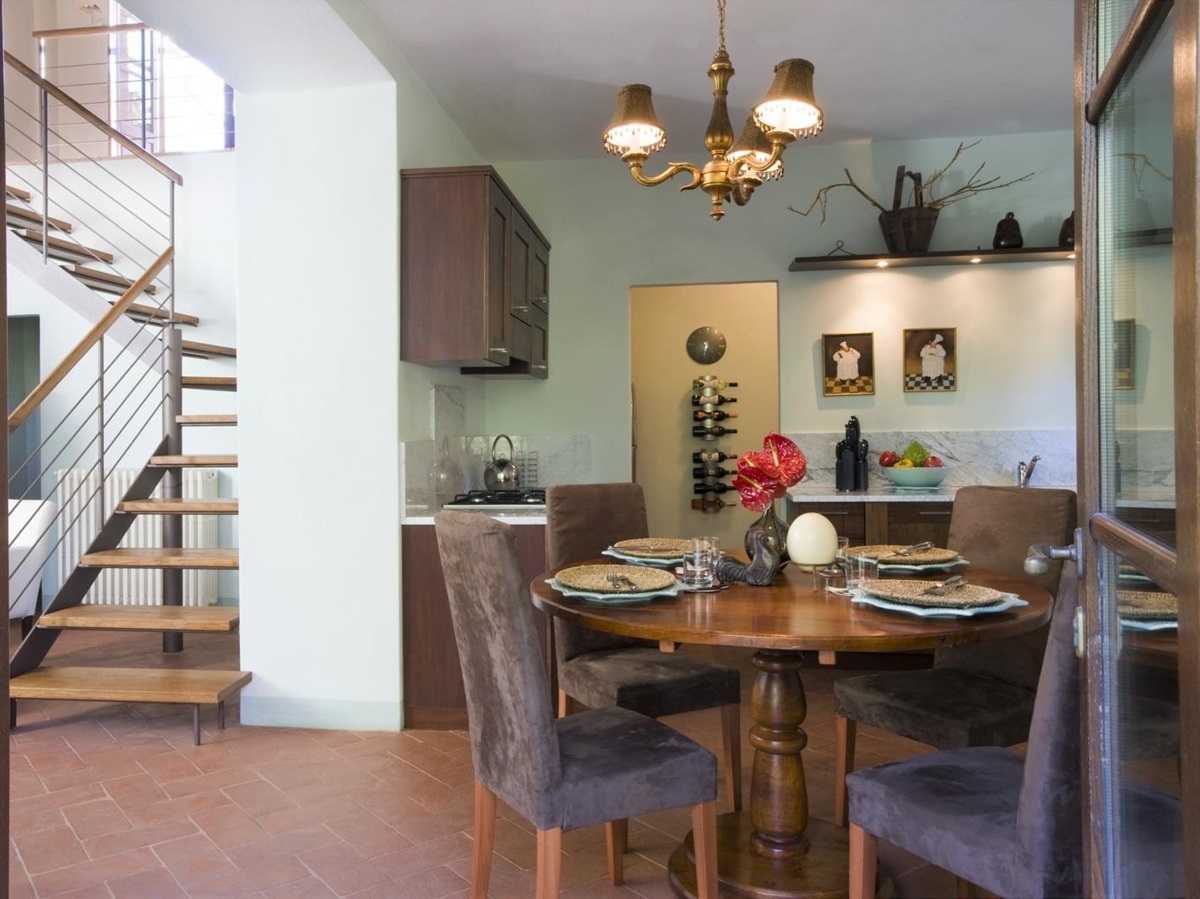 Open plan kitchen and dining area with table, chairs, hanging light and wine store at La Gavelli in Tuscany, Italy