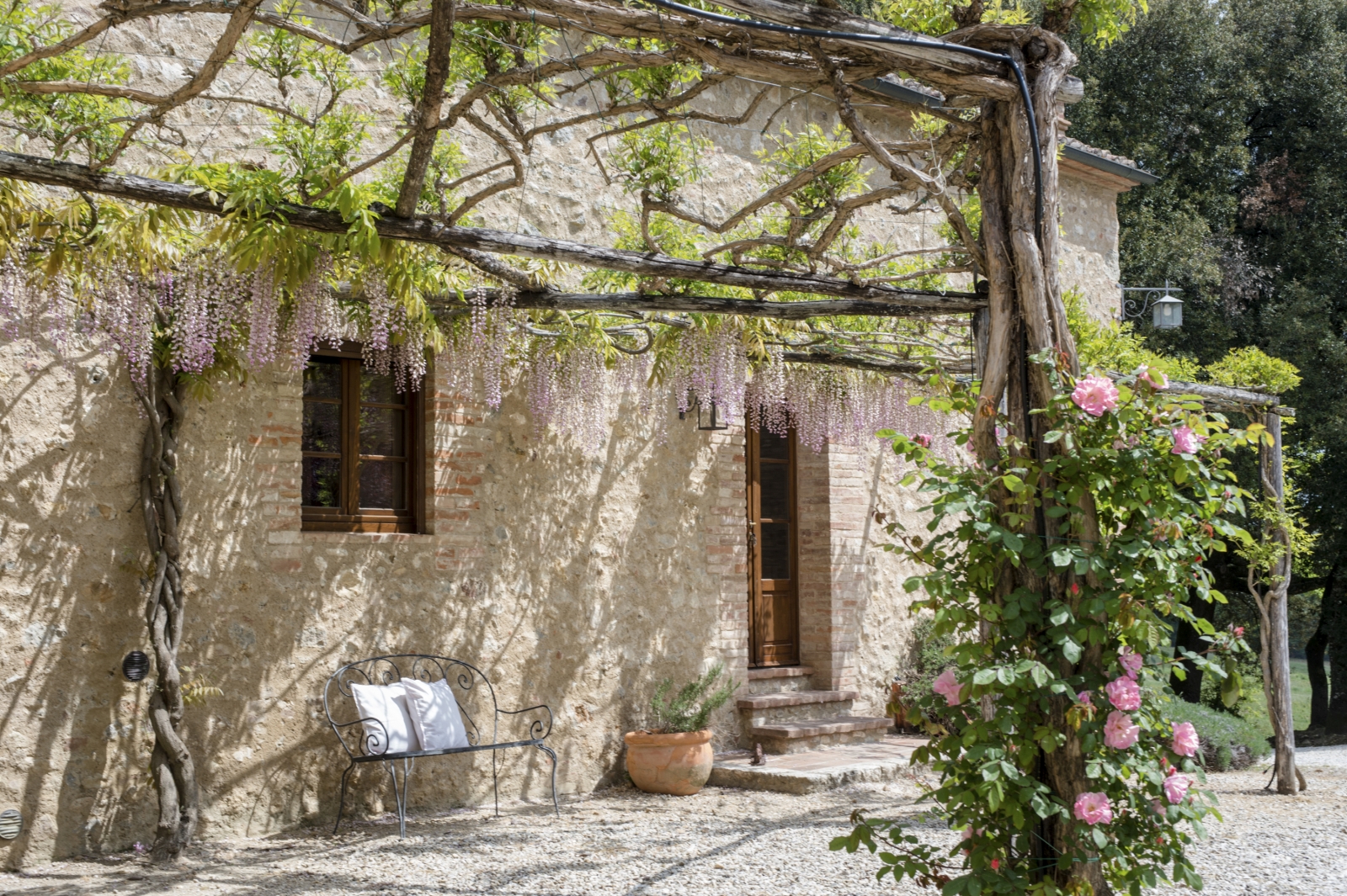 Exterior of villa with arbours, flowers, plants and bench at La Gavelli in Tuscany, Italy