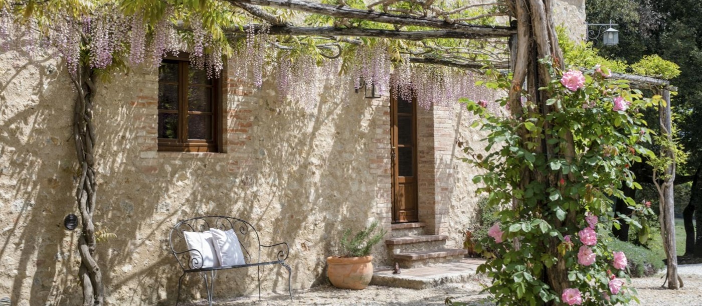 Exterior of villa with arbours, flowers, plants and bench at La Gavelli in Tuscany, Italy