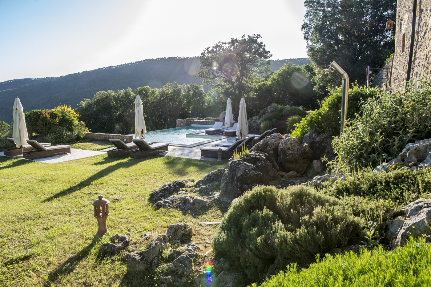 Garden and pool area with plants, sun loungers, and umbrellas at La Gavelli in Tuscany, Italy