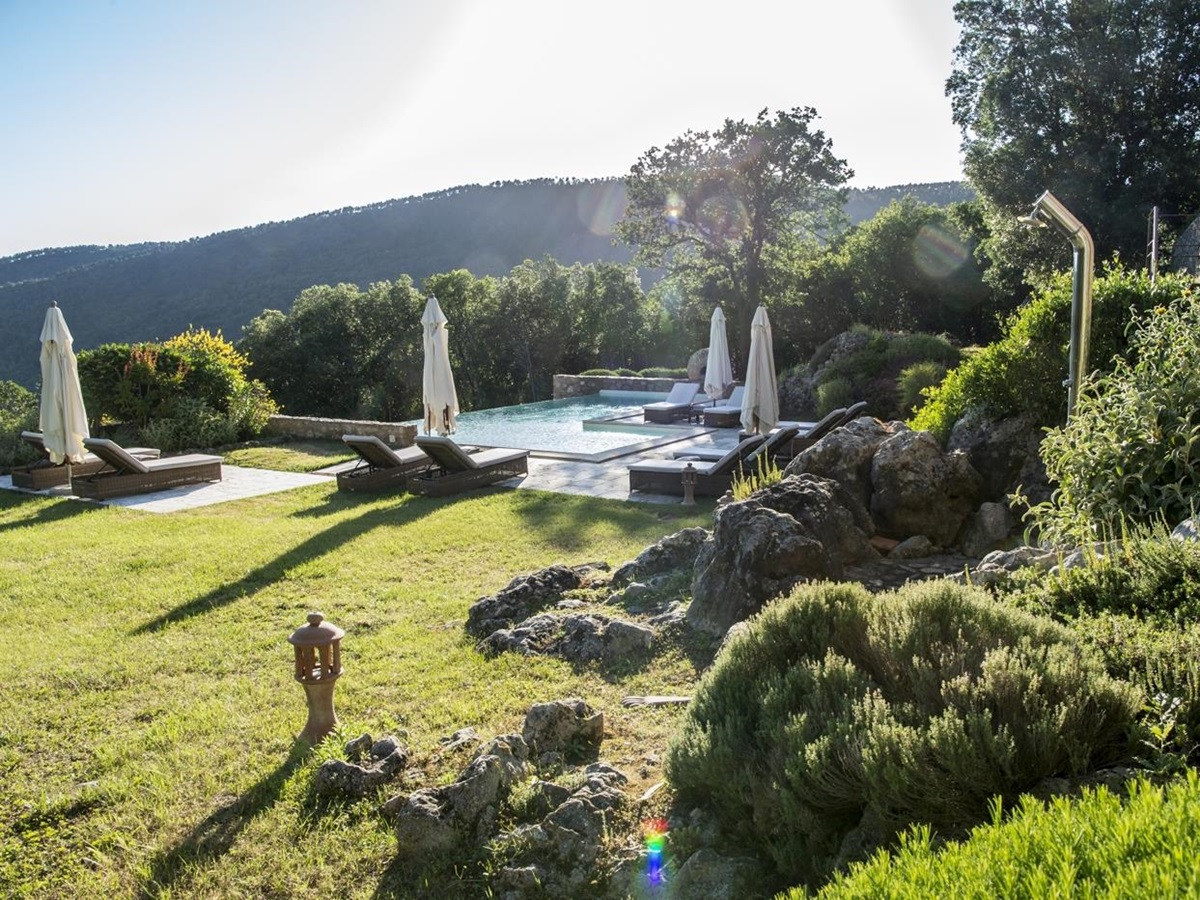 Garden and pool area with plants, sun loungers, and umbrellas at La Gavelli in Tuscany, Italy