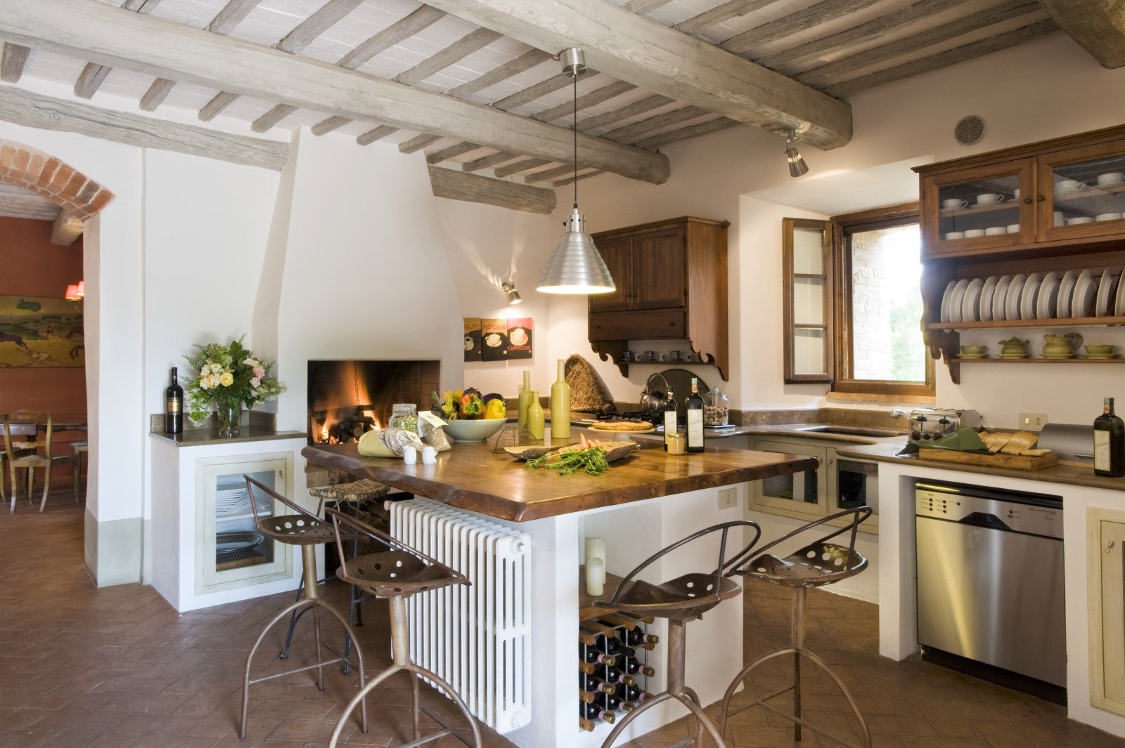 Kitchen with island, chairs, fresh food, hanging light, flowers and fireplace at La Gavelli in Tuscany, Italy
