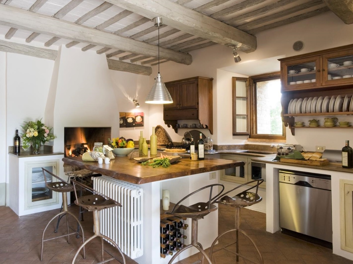 Kitchen with island, chairs, fresh food, hanging light, flowers and fireplace at La Gavelli in Tuscany, Italy