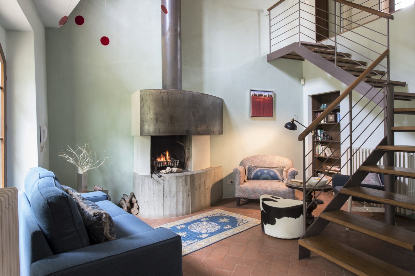 Open plan living area with sofa, fireplace, armchair, bookcase, table and stairs at La Gavelli in Tuscany, Italy