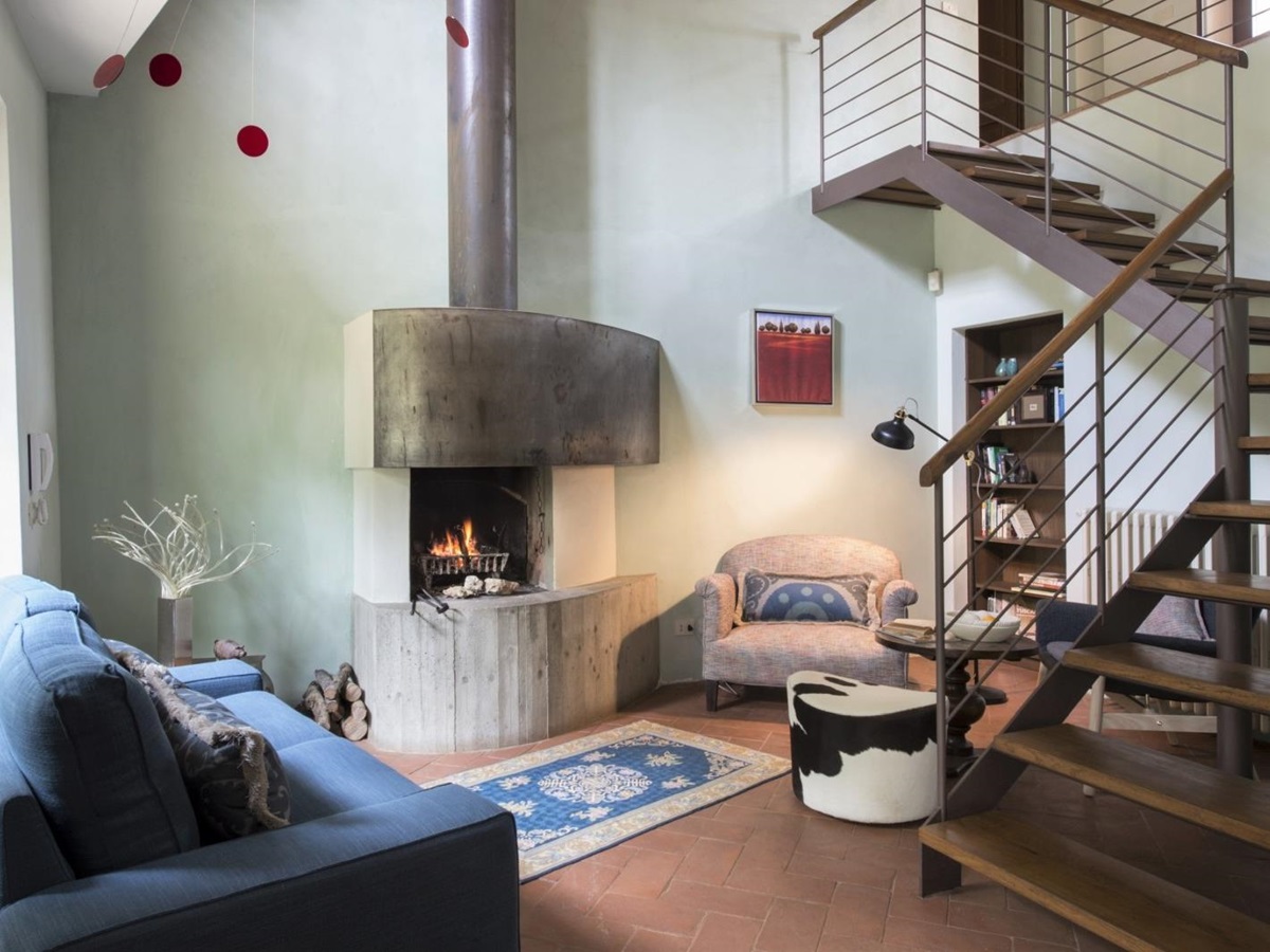 Open plan living area with sofa, fireplace, armchair, bookcase, table and stairs at La Gavelli in Tuscany, Italy