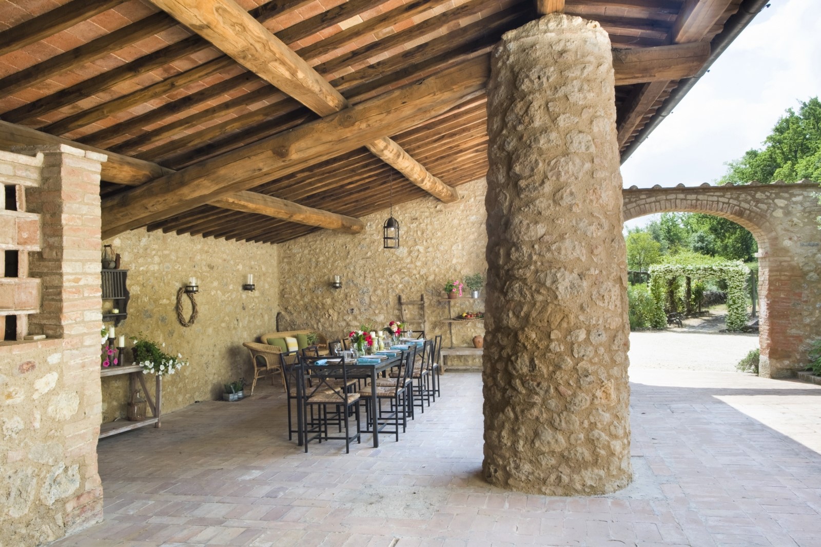 Covered outdoor dining area with pillar, dining table, chairs, flowers and lanterns at La Gavelli in Tuscany, Italy