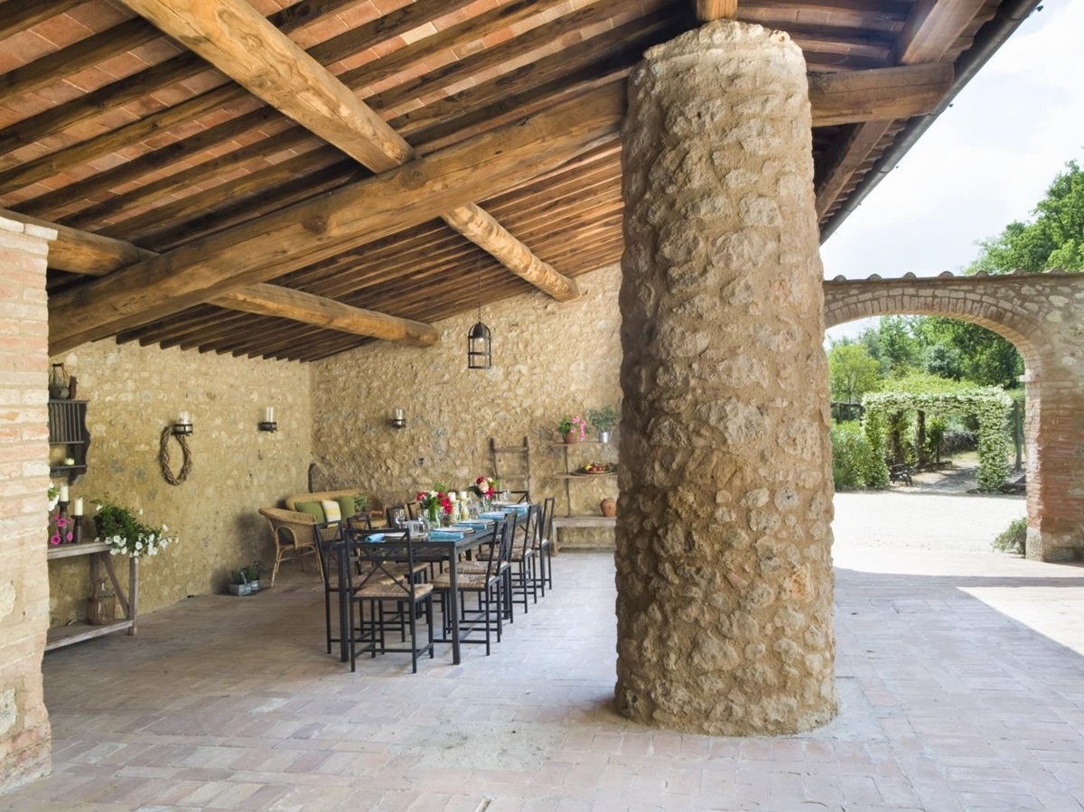 Covered outdoor dining area with pillar, dining table, chairs, flowers and lanterns at La Gavelli in Tuscany, Italy