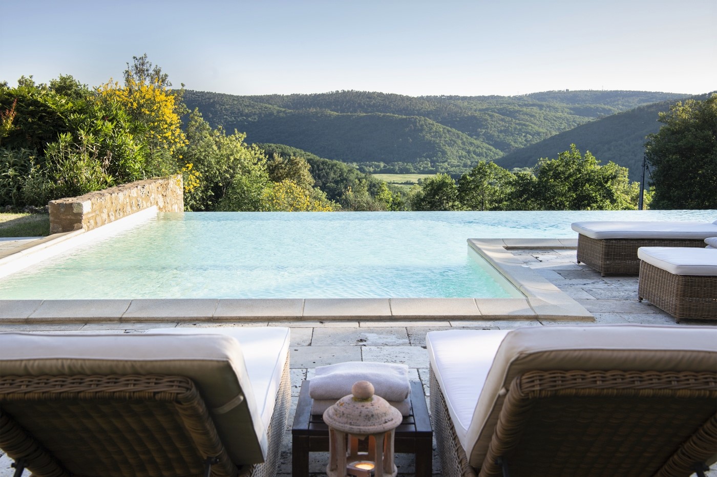 Pool area with infinity pool, sun loungers, lantern and view at La Gavelli in Tuscany, Italy