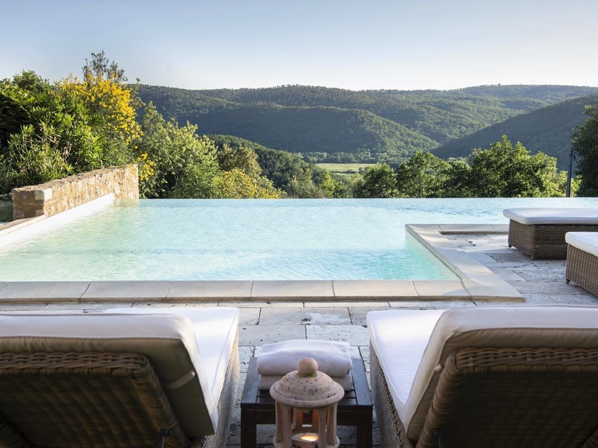 Pool area with infinity pool, sun loungers, lantern and view at La Gavelli in Tuscany, Italy