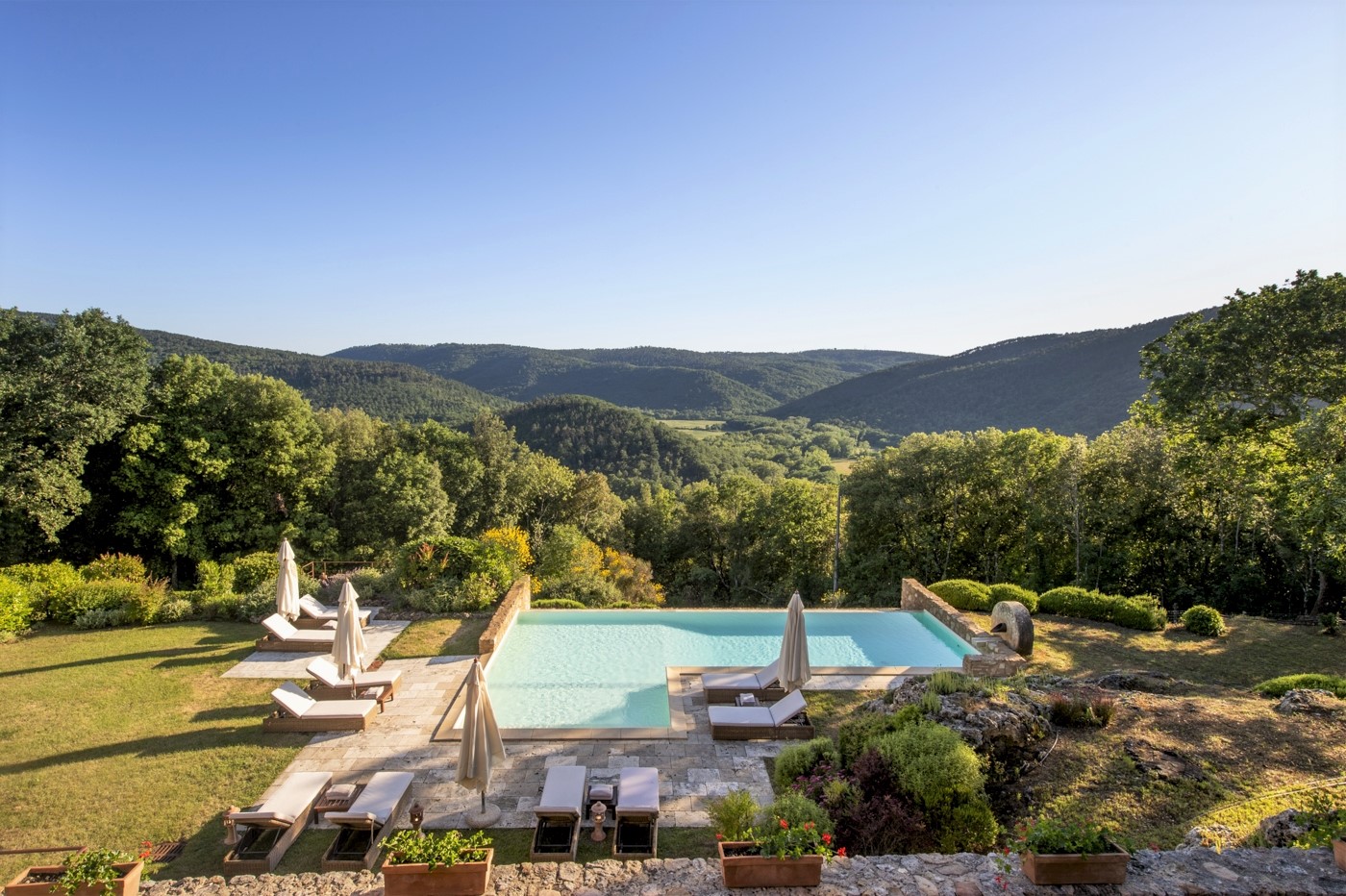 View of infinity pool with sun loungers, umbrellas, flowers and view at La Gavelli in Tuscany, Italy