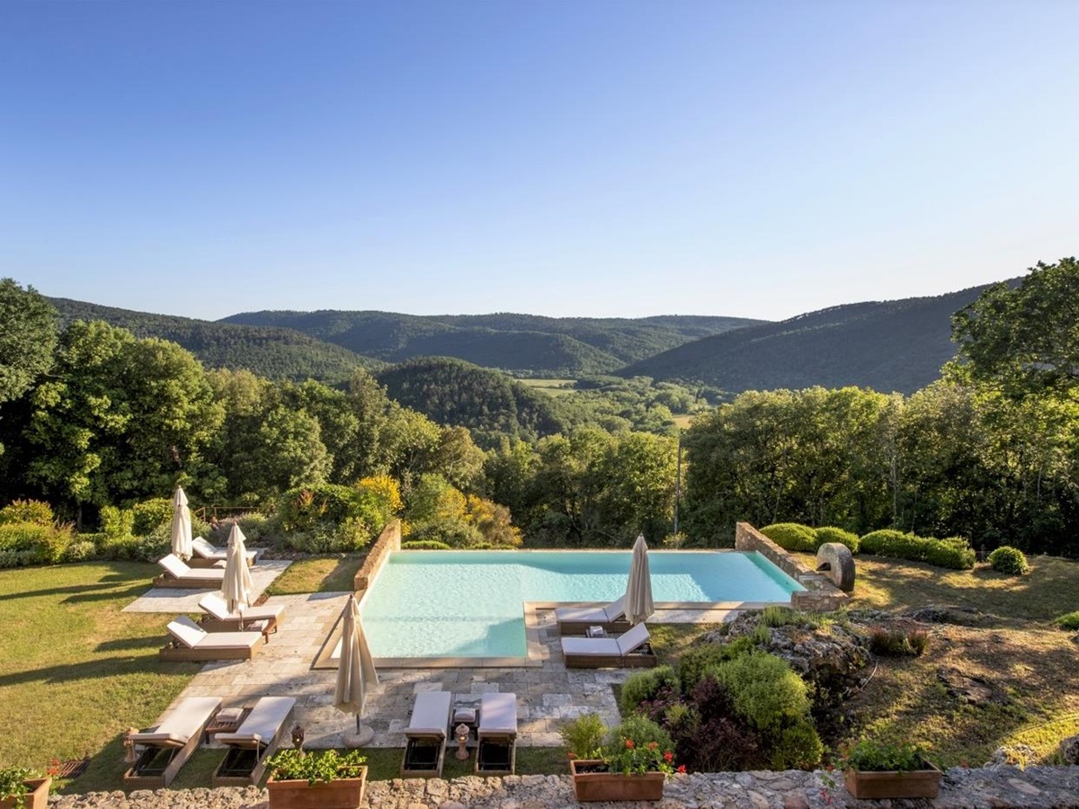 View of infinity pool with sun loungers, umbrellas, flowers and view at La Gavelli in Tuscany, Italy