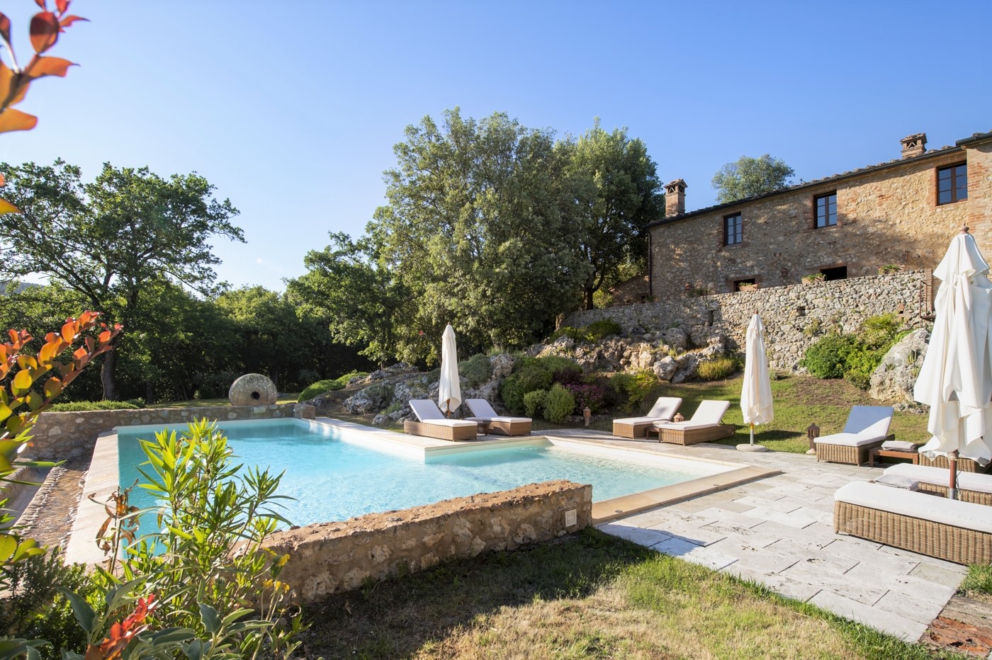 Infinity pool with sun loungers, umbrellas, plants and view of villa at La Gavelli in Tuscany, Italy