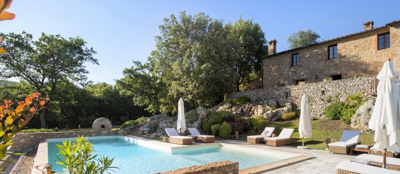 Infinity pool with sun loungers, umbrellas, plants and view of villa at La Gavelli in Tuscany, Italy