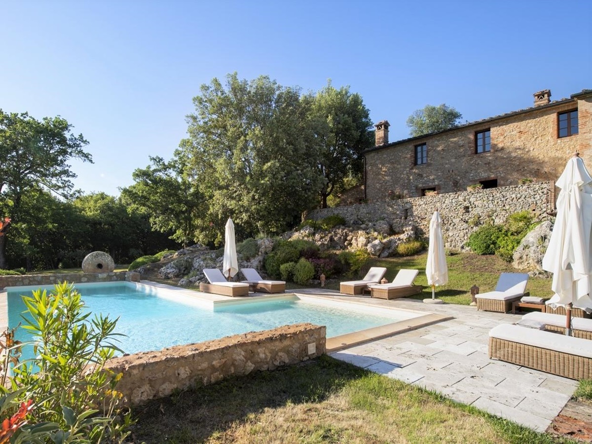 Infinity pool with sun loungers, umbrellas, plants and view of villa at La Gavelli in Tuscany, Italy