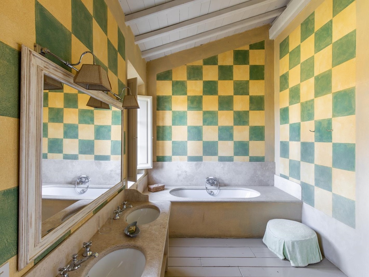 Bathroom with yellow & green walls, two sinks, large mirror, window and bath at La Vigna in Tuscany, Italy
