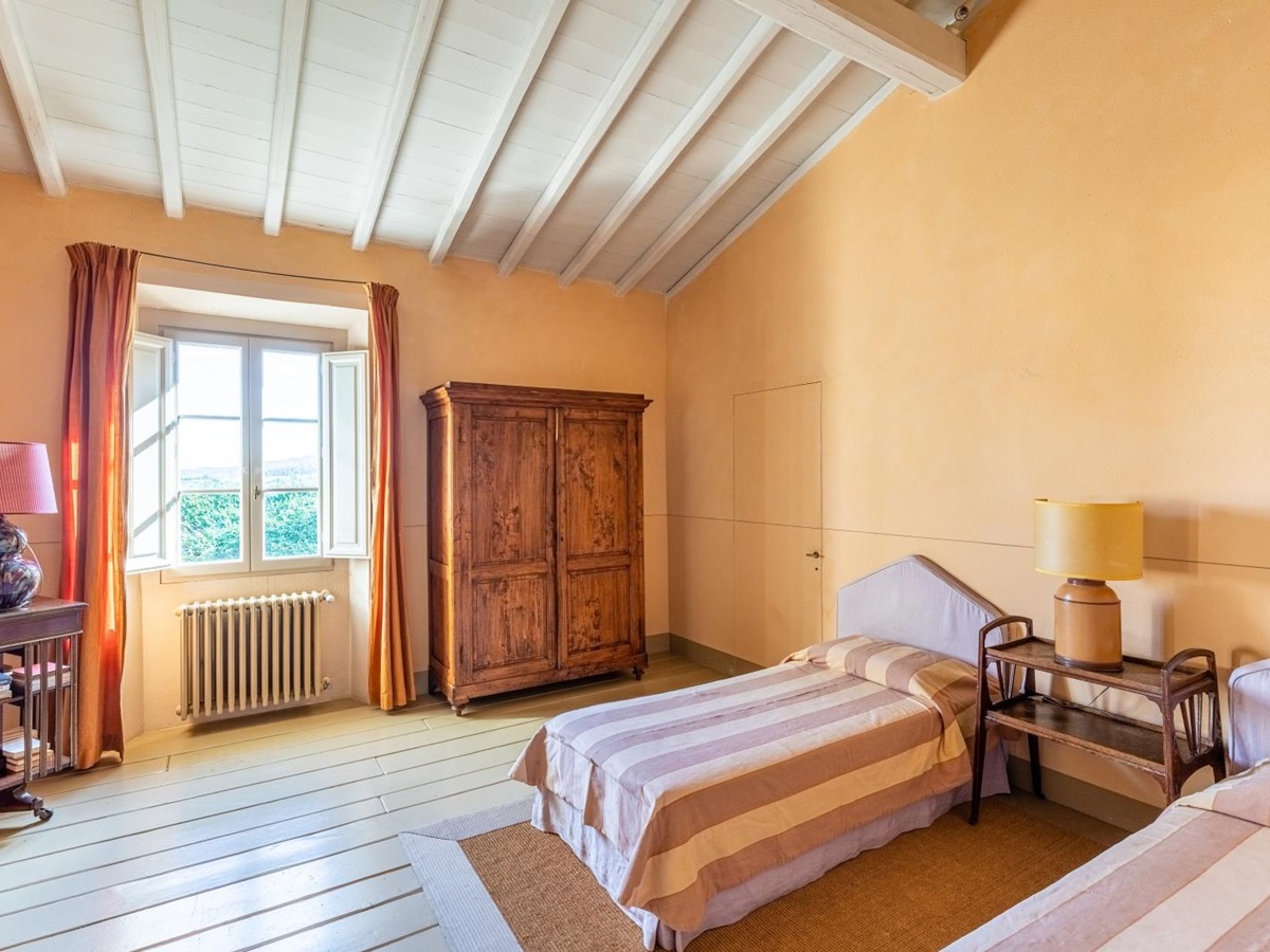 Bedroom with twin beds, bedside table, lamp, wardrobe, window and small table at La Vigna in Tuscany, Italy