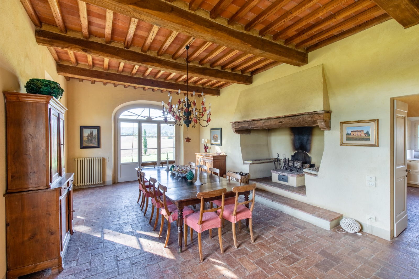 Dining room with cabinet, dining table, chairs, candles, chandelier, fireplace and French doors at La Vigna in Tuscany, Italy