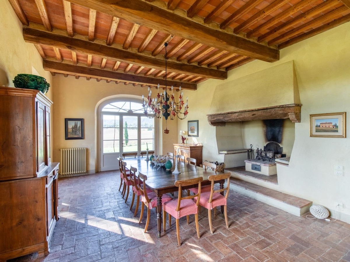 Dining room with cabinet, dining table, chairs, candles, chandelier, fireplace and French doors at La Vigna in Tuscany, Italy