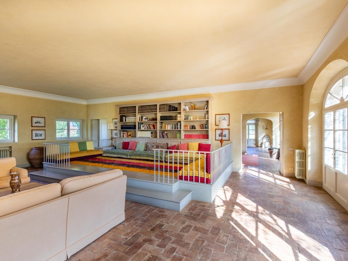 Living room with sofas, colourful elevated sitting area, bookshelves, lamps and French doors at La Vigna in Tuscany, Italy