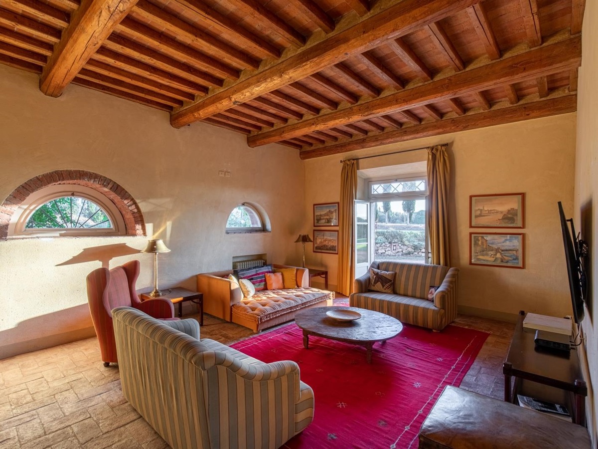Living room with pink rug, coffee table, sofas, armchair, TV and French doors to garden at La Vigna in Tuscany, Italy