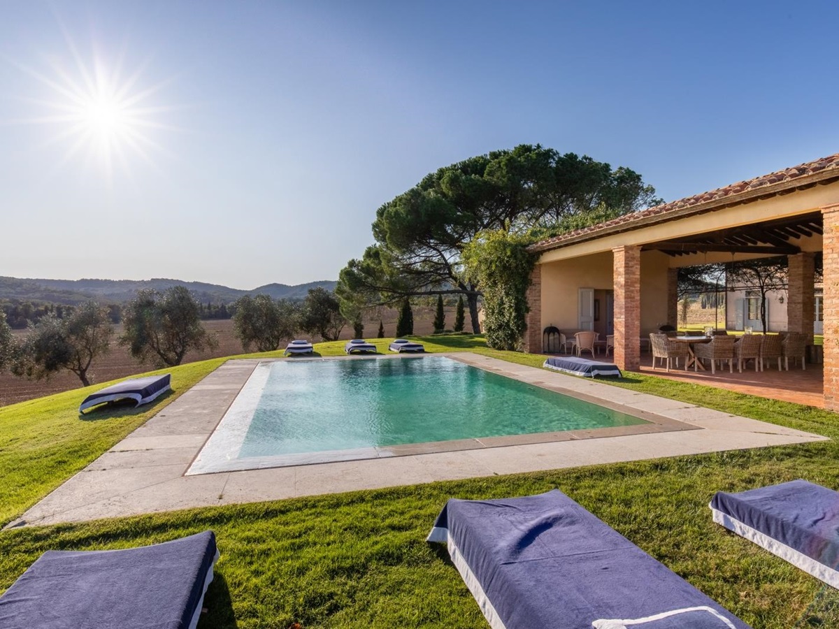 Pool area with sun loungers and covered outdoor dining area in garden at La Vigna in Tuscany, Italy