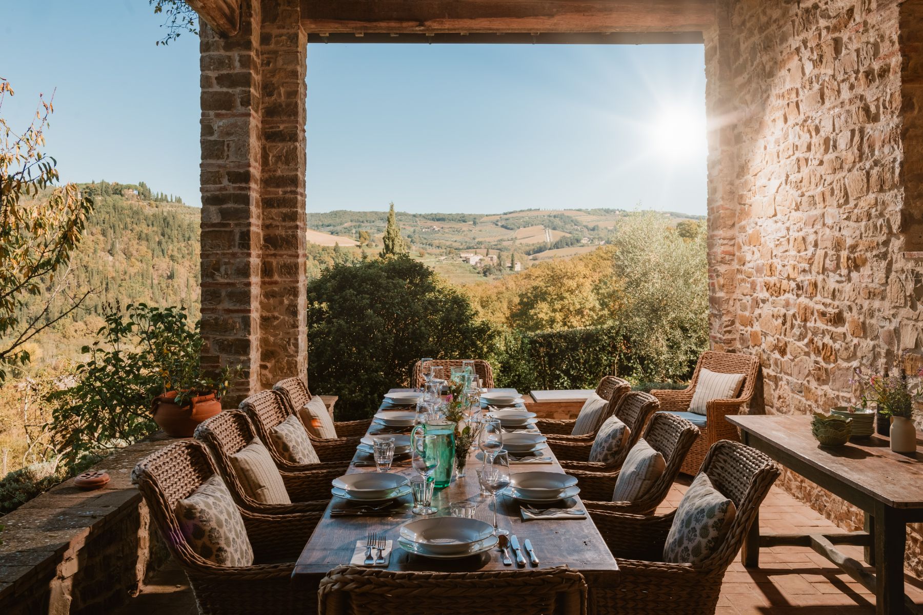 Long wooden outdoor dining table with wicker chairs and views of Tuscany at Podere Cipressi