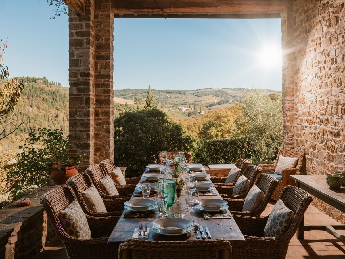 Long wooden outdoor dining table with wicker chairs and views of Tuscany at Podere Cipressi