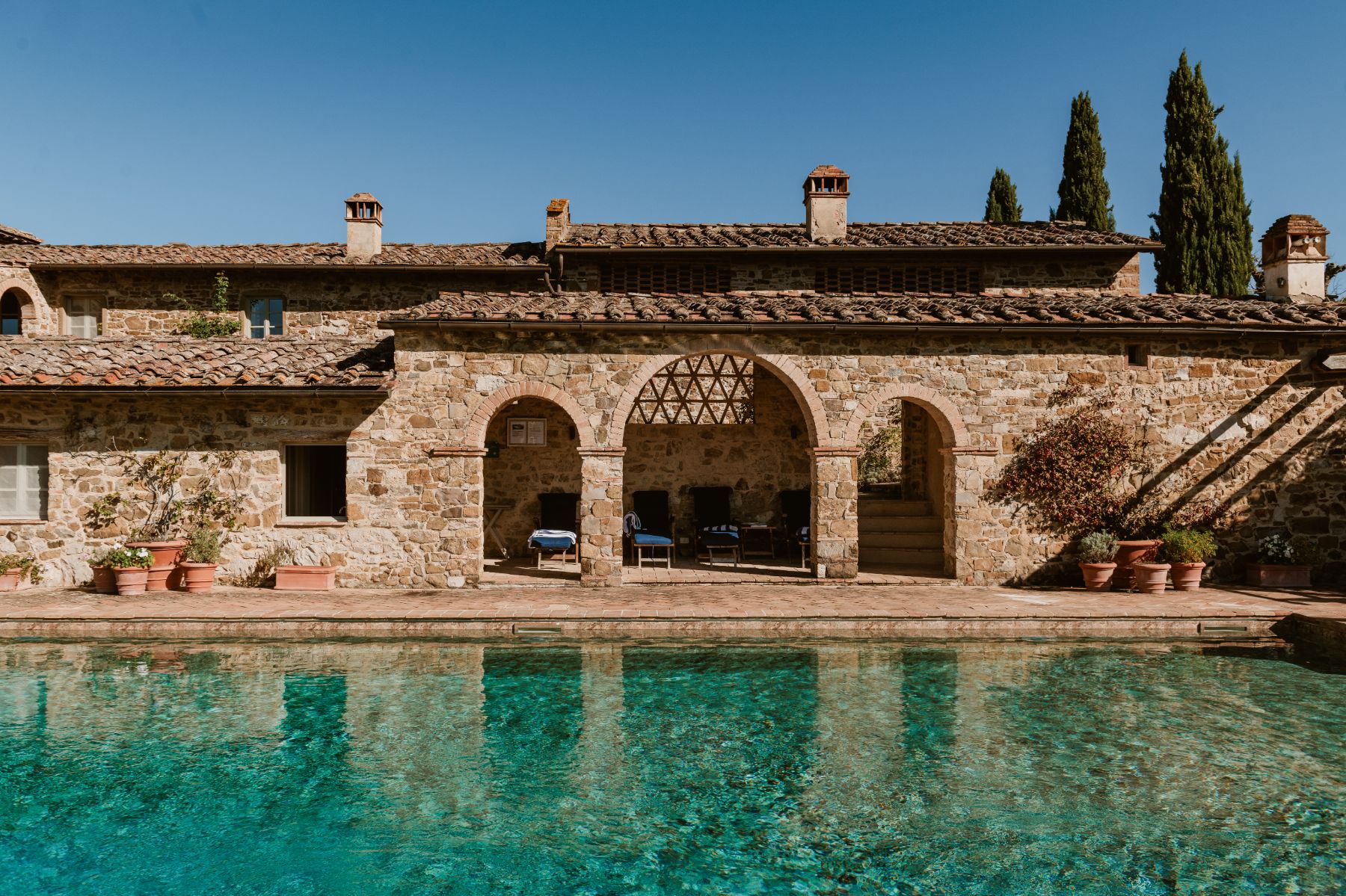 View of the outdoor swimming pool with sun loungers at Podere Cipressi in Tuscany
