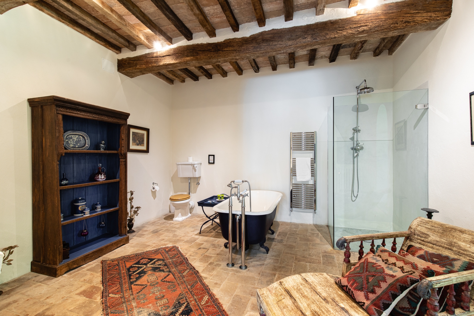Bathroom with shelves, rug, painting, toilet, bath, towel rail, shower and chair at Tenuta Cantata in Tuscany, Italy
