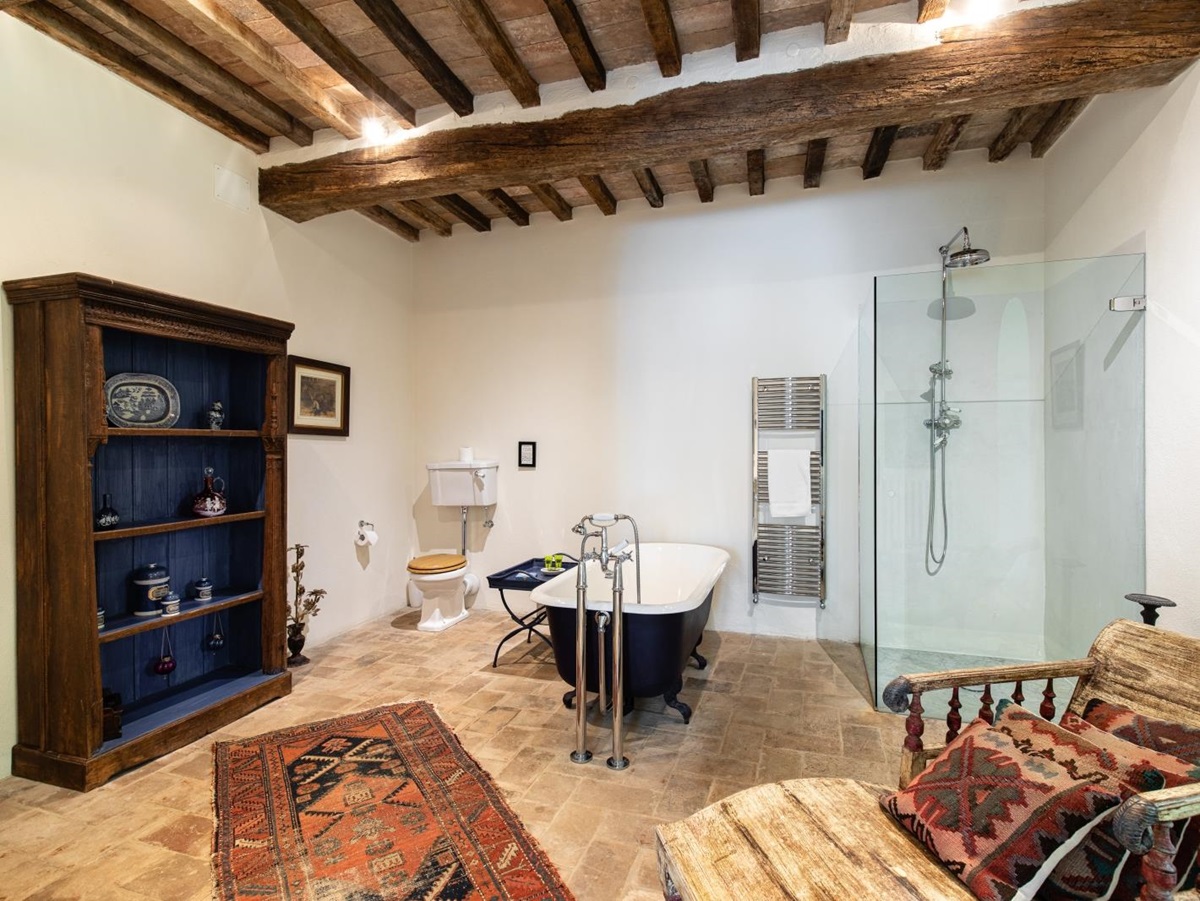 Bathroom with shelves, rug, painting, toilet, bath, towel rail, shower and chair at Tenuta Cantata in Tuscany, Italy