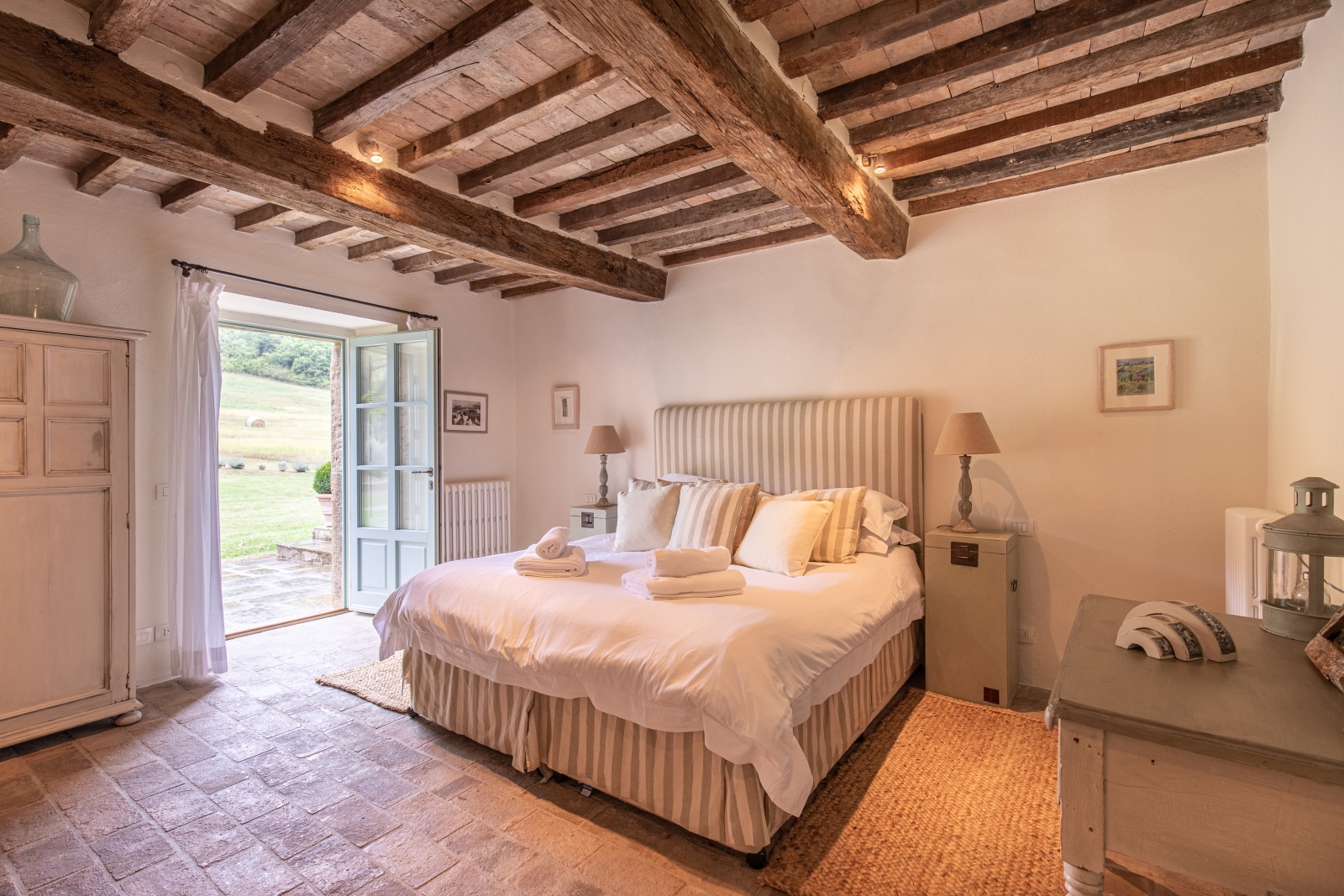 Bedroom with double bed, bedside tables, lamps, pictures, French doors and ceiling beams at Tenuta Cantata in Tuscany, Italy