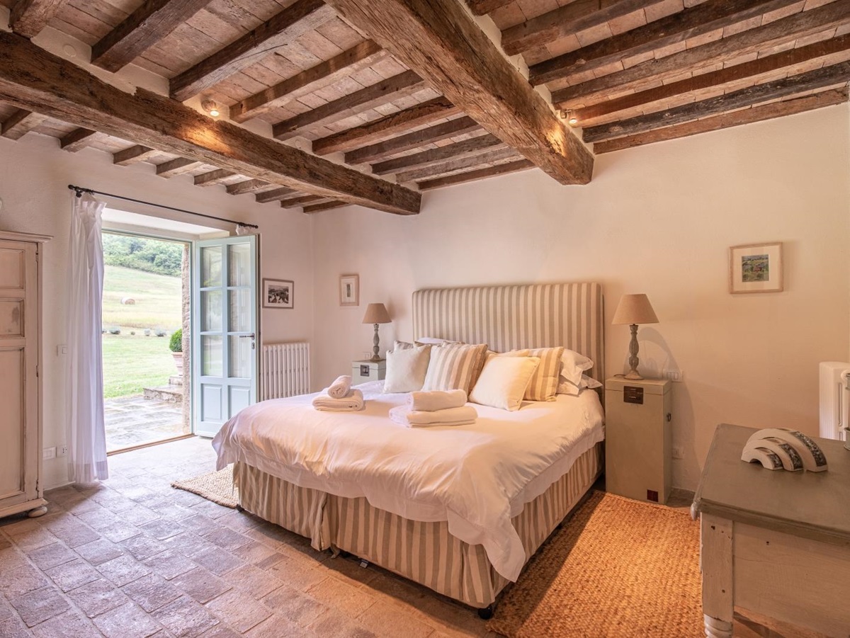 Bedroom with double bed, bedside tables, lamps, pictures, French doors and ceiling beams at Tenuta Cantata in Tuscany, Italy