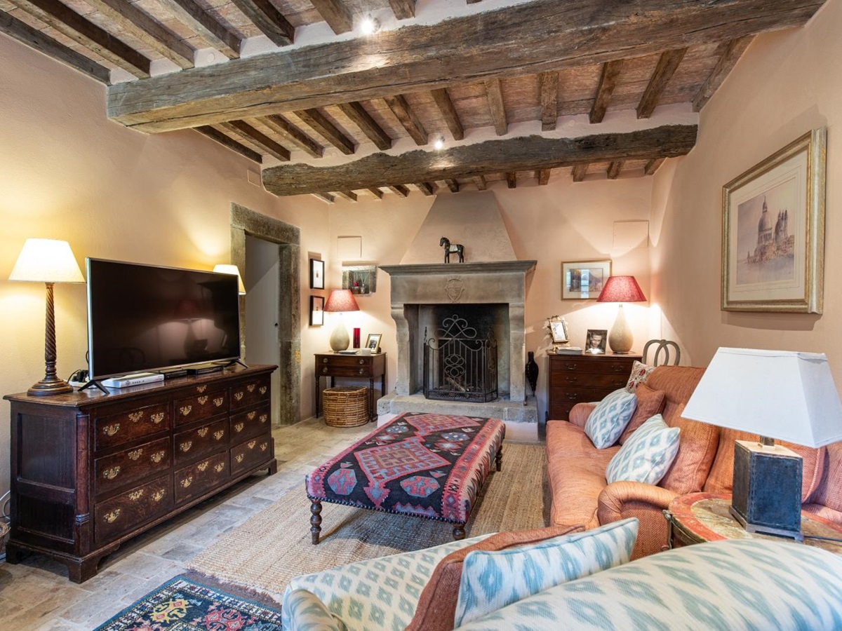 Living room with TV, sofa, armchair, footstool, artwork, cabinets, lamps and fireplace at Tenuta Cantata in Tuscany, Italy