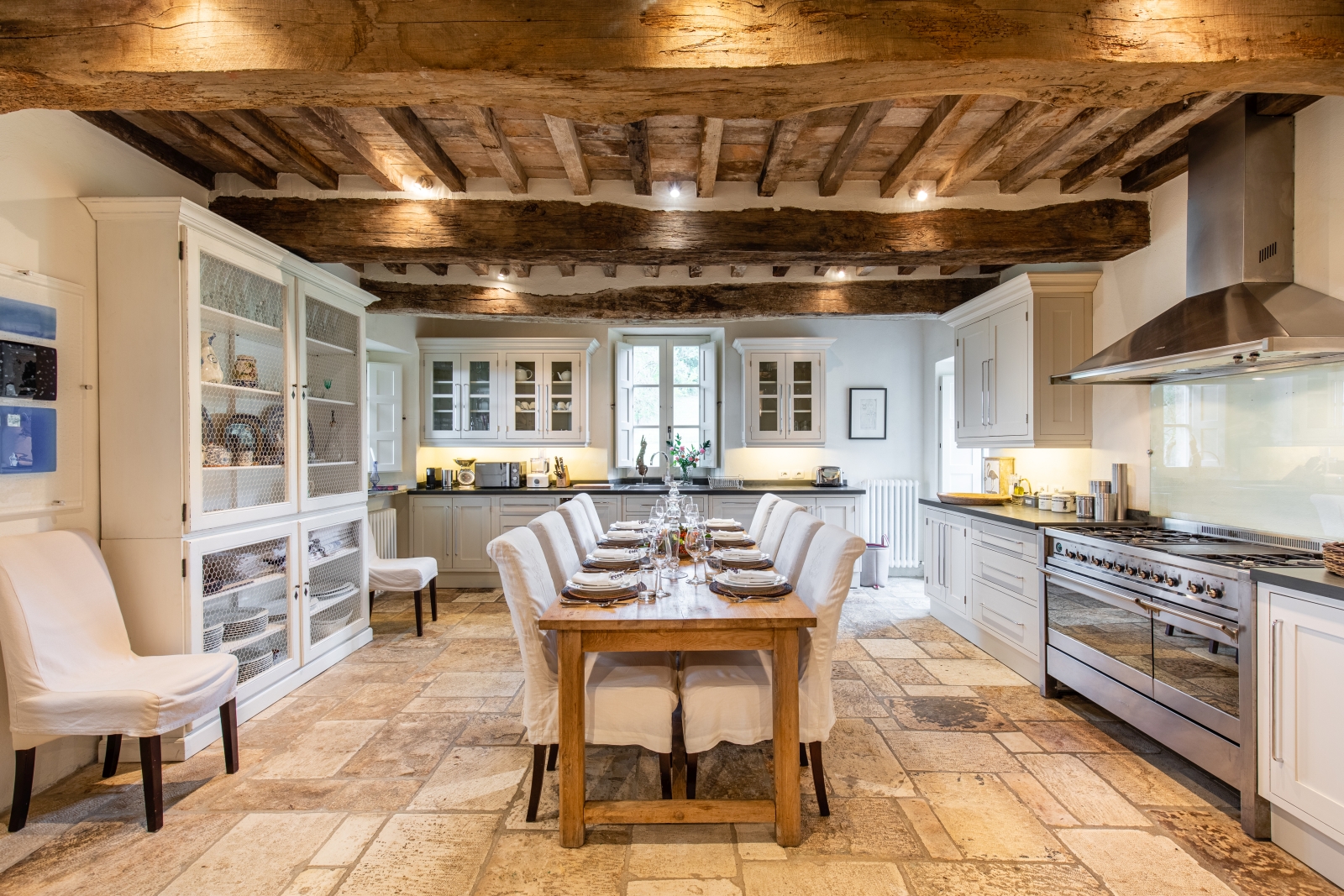 Kitchen with long table, comfy chairs, crockery, appliances, cupboards and ceiling beams at Tenuta Cantata in Tuscany, Italy