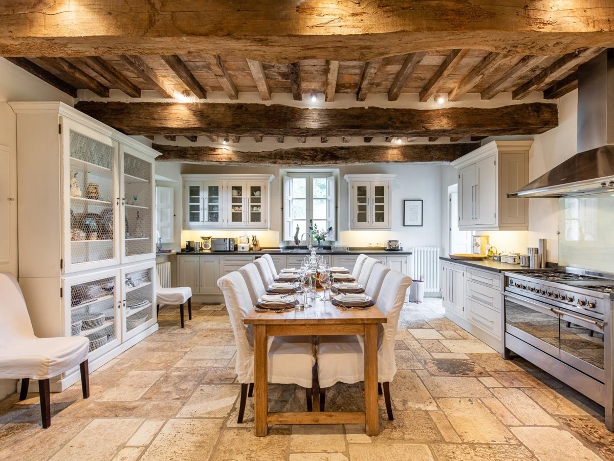 Kitchen with long table, comfy chairs, crockery, appliances, cupboards and ceiling beams at Tenuta Cantata in Tuscany, Italy
