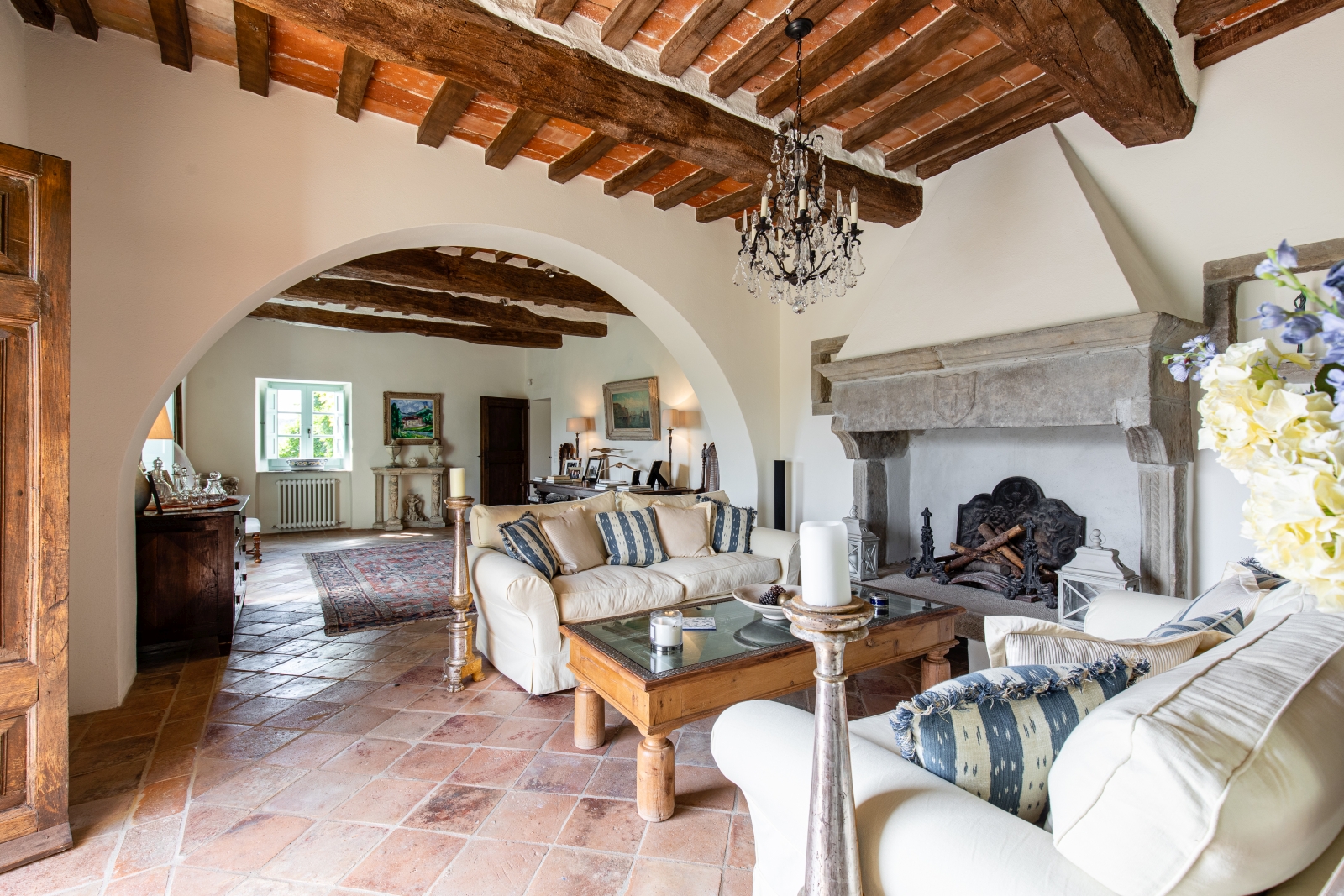 Living room with candle, sofas, coffee table, flowers, chandelier, fireplace & paintings at Tenuta Cantata in Tuscany, Italy
