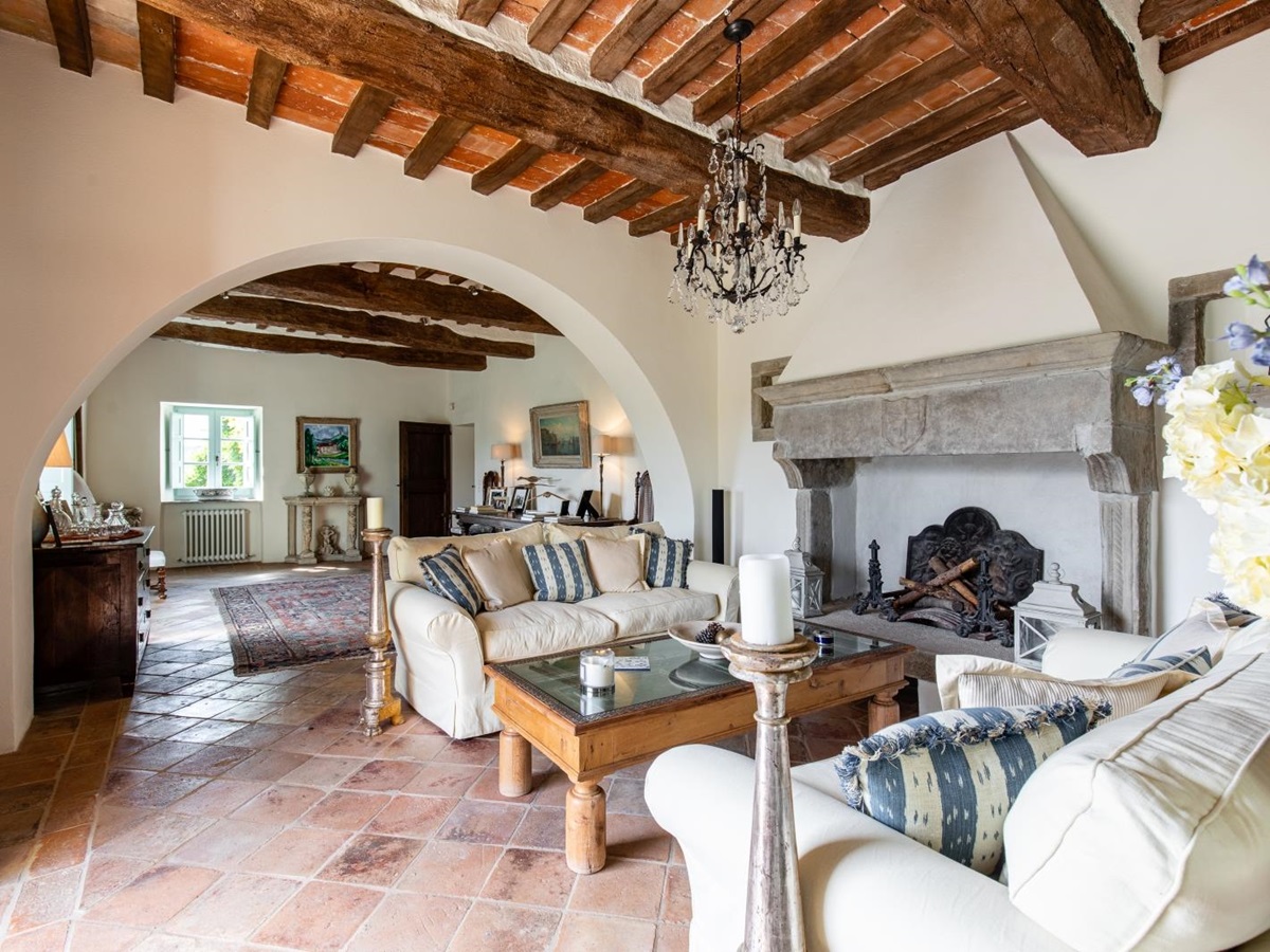 Living room with candle, sofas, coffee table, flowers, chandelier, fireplace & paintings at Tenuta Cantata in Tuscany, Italy