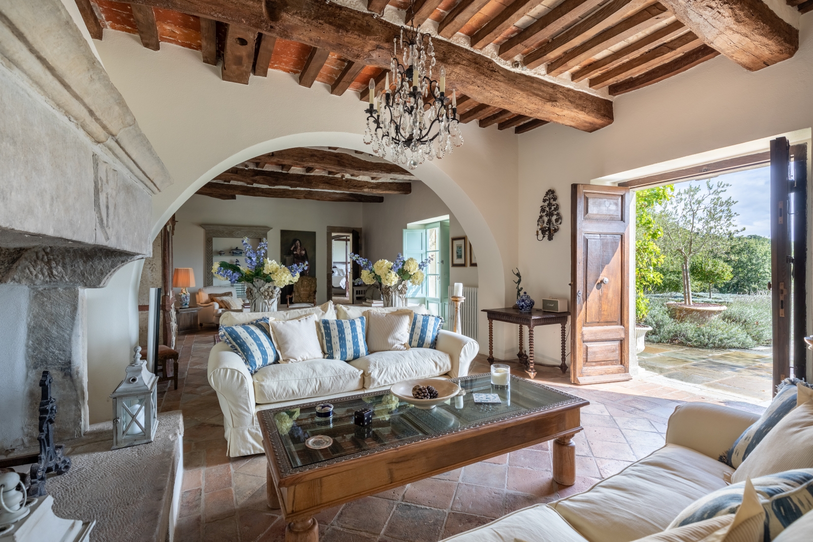 Lounge with sofas, coffee table, fireplace, flowers, chandelier and doors to garden at Tenuta Cantata in Tuscany, Italy