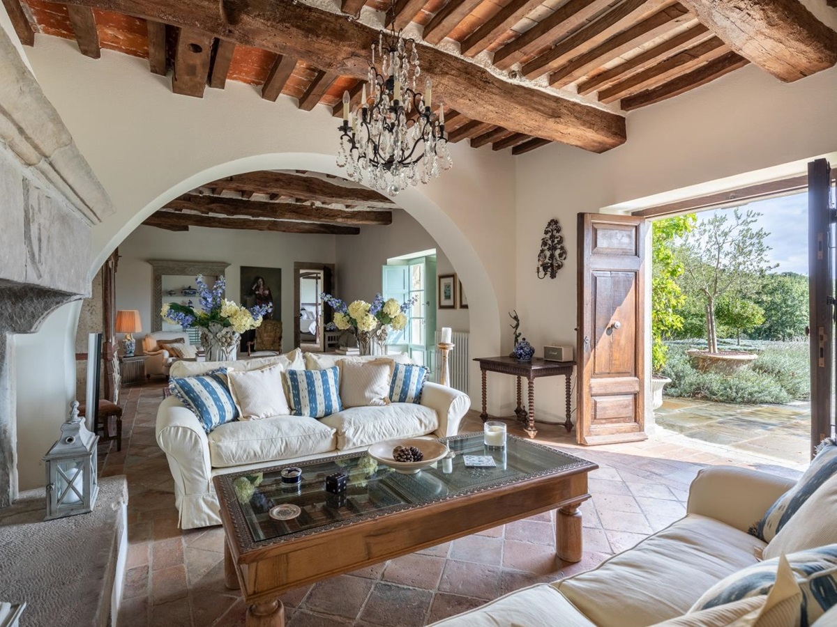 Lounge with sofas, coffee table, fireplace, flowers, chandelier and doors to garden at Tenuta Cantata in Tuscany, Italy