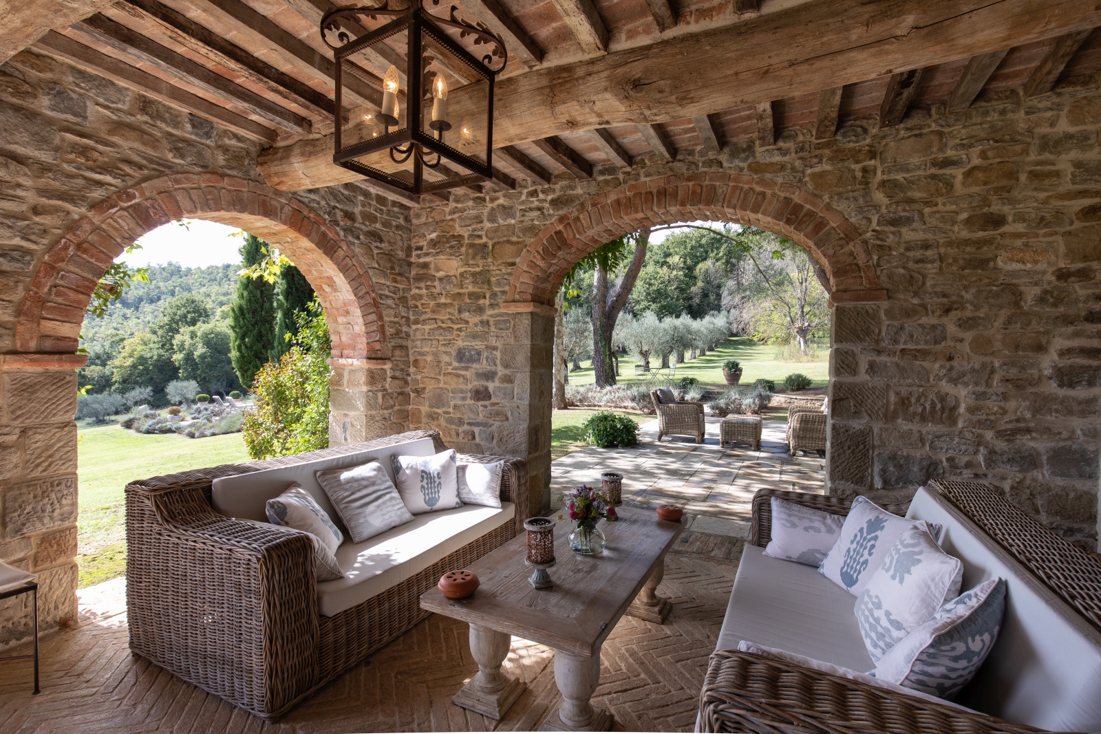 Outdoor lounge area with loggia, sofas, coffee table, light and view to patio and garden at Tenuta Cantata in Tuscany, Italy