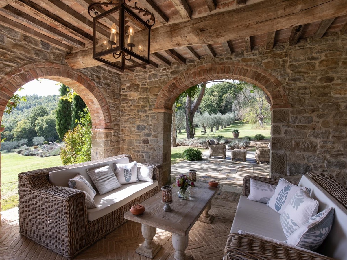 Outdoor lounge area with loggia, sofas, coffee table, light and view to patio and garden at Tenuta Cantata in Tuscany, Italy