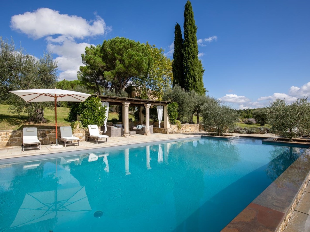 Pool with patio area, sun loungers, covered lounge area, trees and view of garden at Tenuta Cantata in Tuscany, Italy