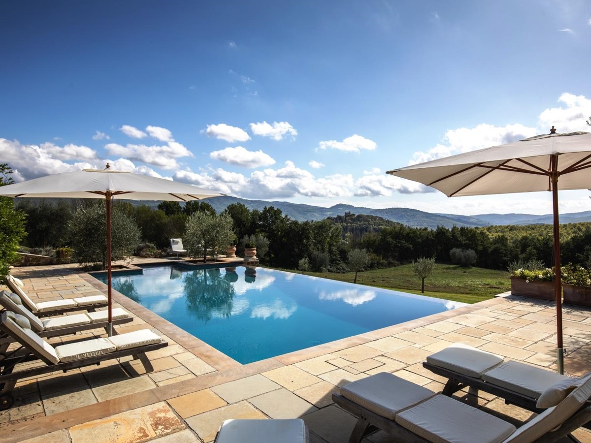 Pool area with patio, sun loungers, umbrellas, flowers, trees and countryside view at Tenuta Cantata in Tuscany, Italy
