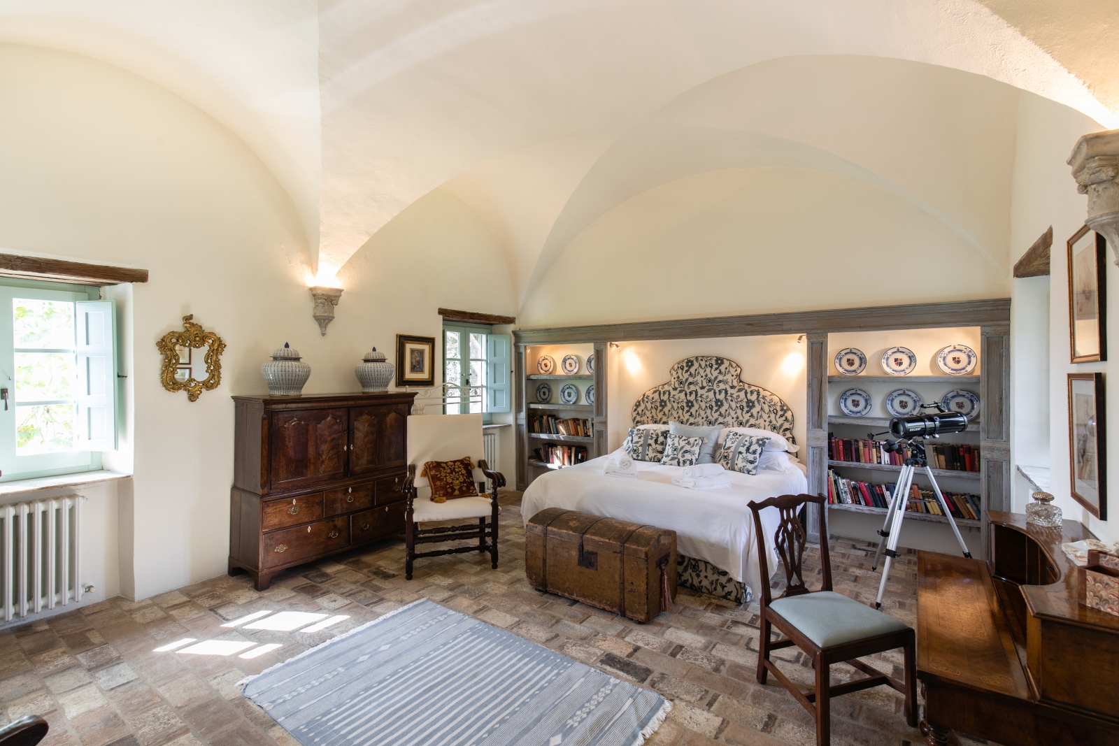 Bedroom with double bed, chest, chairs, desk, books, plates, telescope and cabinet at Tenuta Cantata in Tuscany, Italy