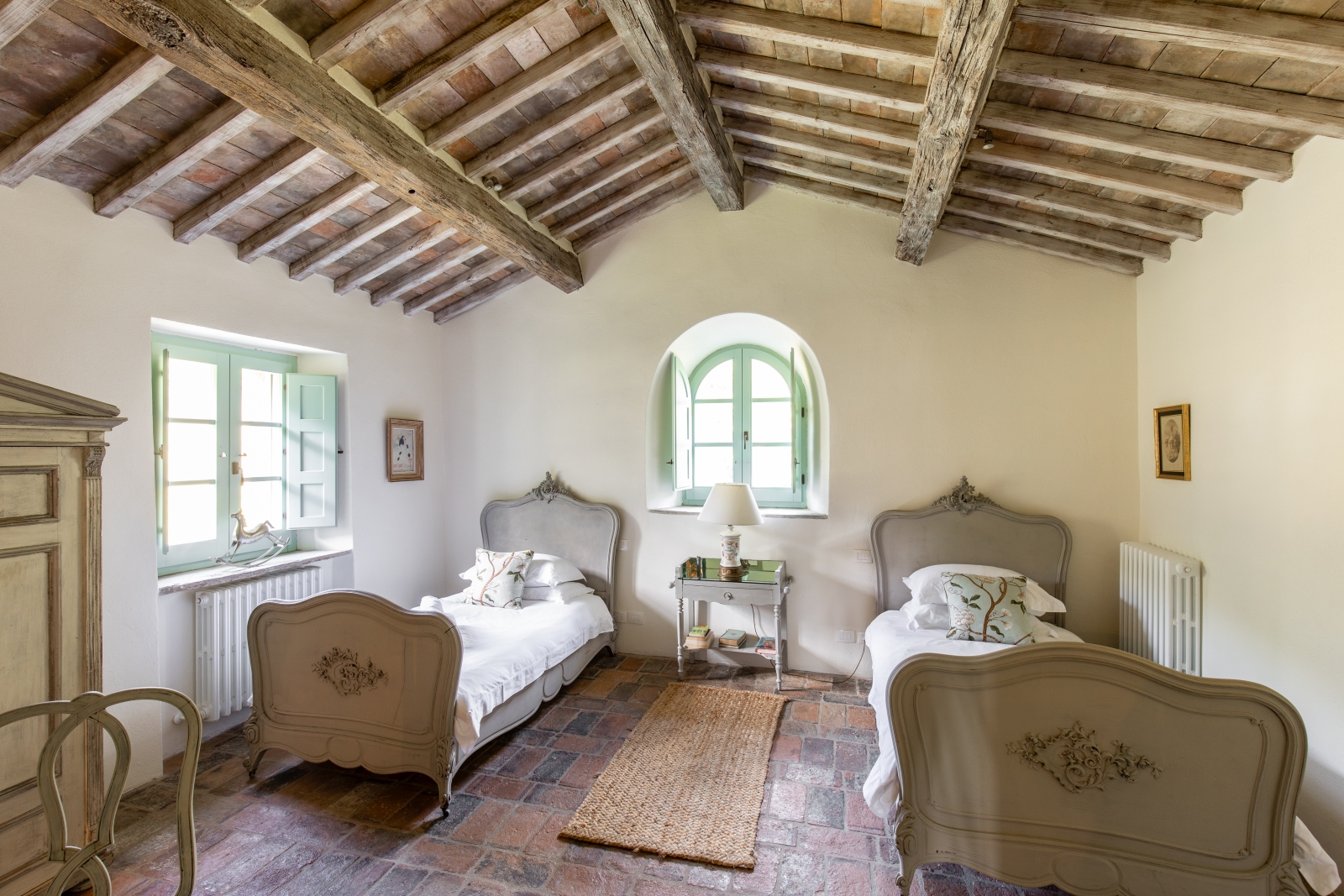 Bedroom with twin beds, bedside table, lamp, rug, windows, wardrobe and ceiling beams at Tenuta Cantata in Tuscany, Italy