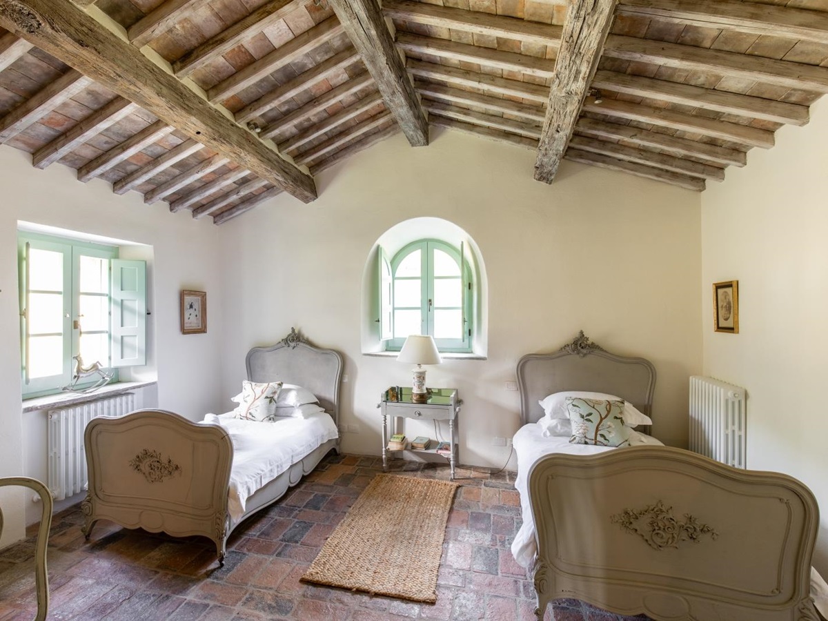 Bedroom with twin beds, bedside table, lamp, rug, windows, wardrobe and ceiling beams at Tenuta Cantata in Tuscany, Italy